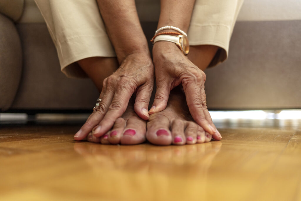 An older woman massages her feet to relieve the pain caused by arthritis.